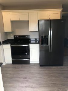 Modern kitchen remodeling in Southern MD.  The photo shows black appliances and white cabinets with a beautiful wood-look laminate floor. 