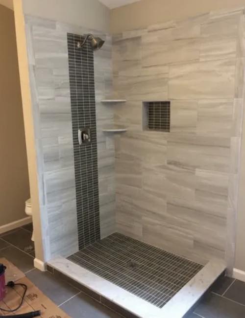 Photo shows Modern shower installation with tile floor and walls, built in shelves and nook. 